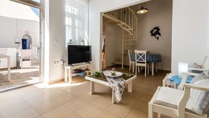 A spacious living room with a TV, a dining table, and a staircase leading to an upper floor. - Cycladic home in Adamas, Casa Nostalgia, Greece (Milos)
