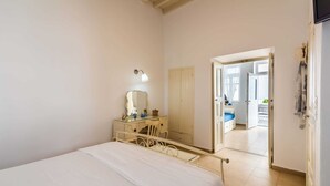 A bedroom with a bed, a dresser with a mirror, and a door leading to a bathroom. - Cycladic home in Adamas, Casa Nostalgia, Greece (Milos)