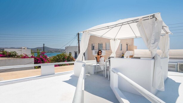A rooftop terrace with a white canopy, outdoor seating, and a view of the sea and buildings. - Cycladic home in Adamas, Casa Nostalgia, Greece (Milos)