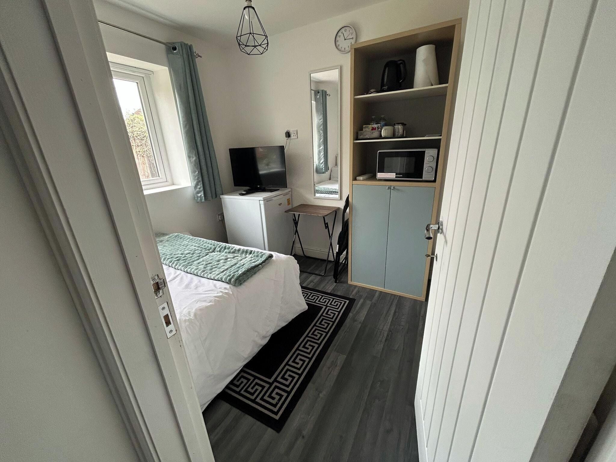 Ein kleines Schlafzimmer mit Bett, Fernseher, Mikrowelle und Kleiderschrank.