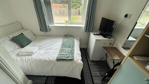 A neatly arranged bedroom with a bed, a desk with a computer, a television, and a window with curtains. - Private Room, Sleeps 2 With Ensuite & Parking (Birmingham)