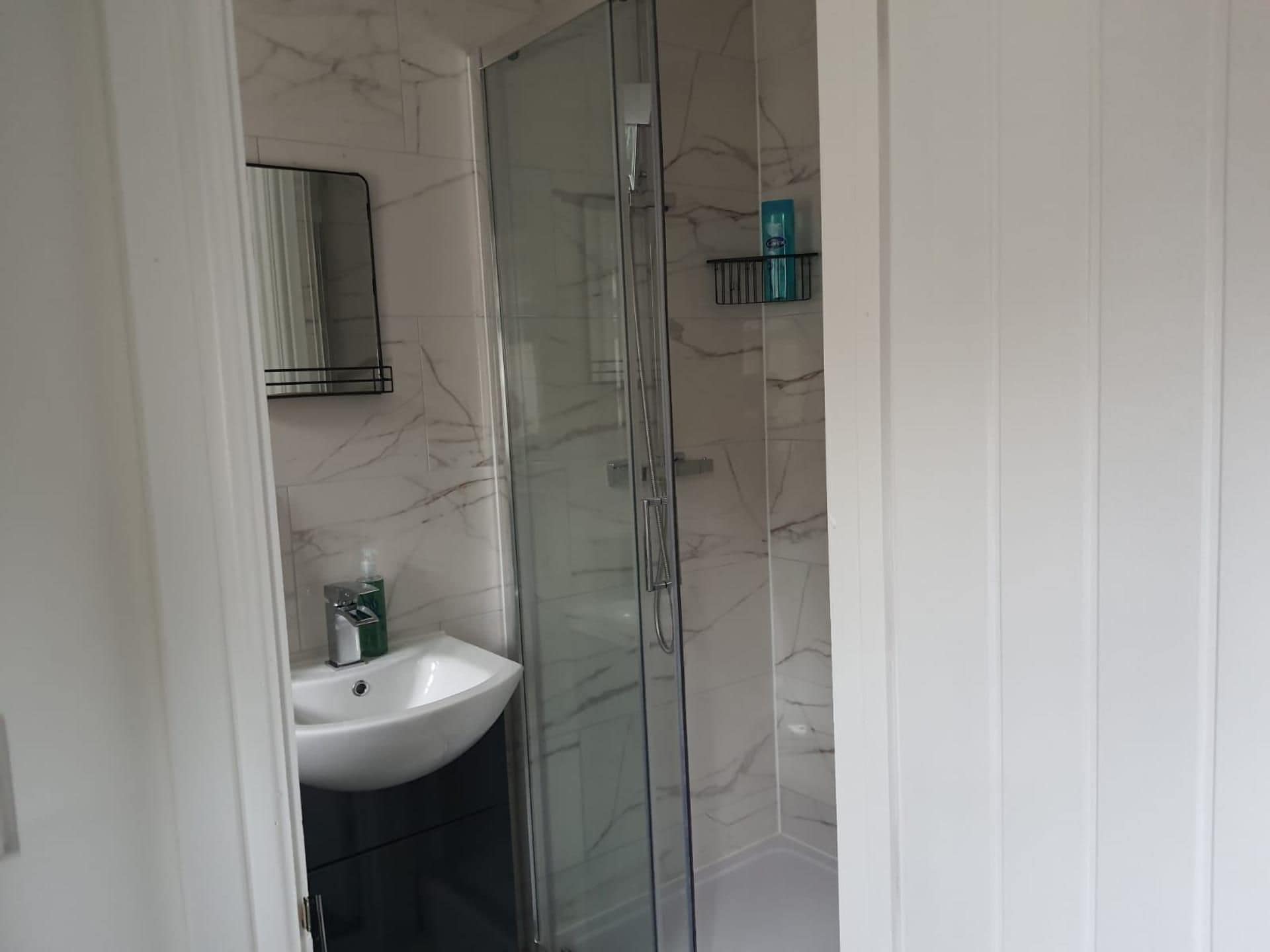 Ein Badezimmer mit weißem Waschbecken, einer Duschkabine aus Glas und einer Wand mit Marmorfliesen.