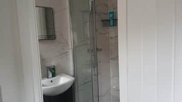 Une salle de bain avec un lavabo blanc, une cabine de douche en verre et un mur recouvert de carreaux de marbre.
