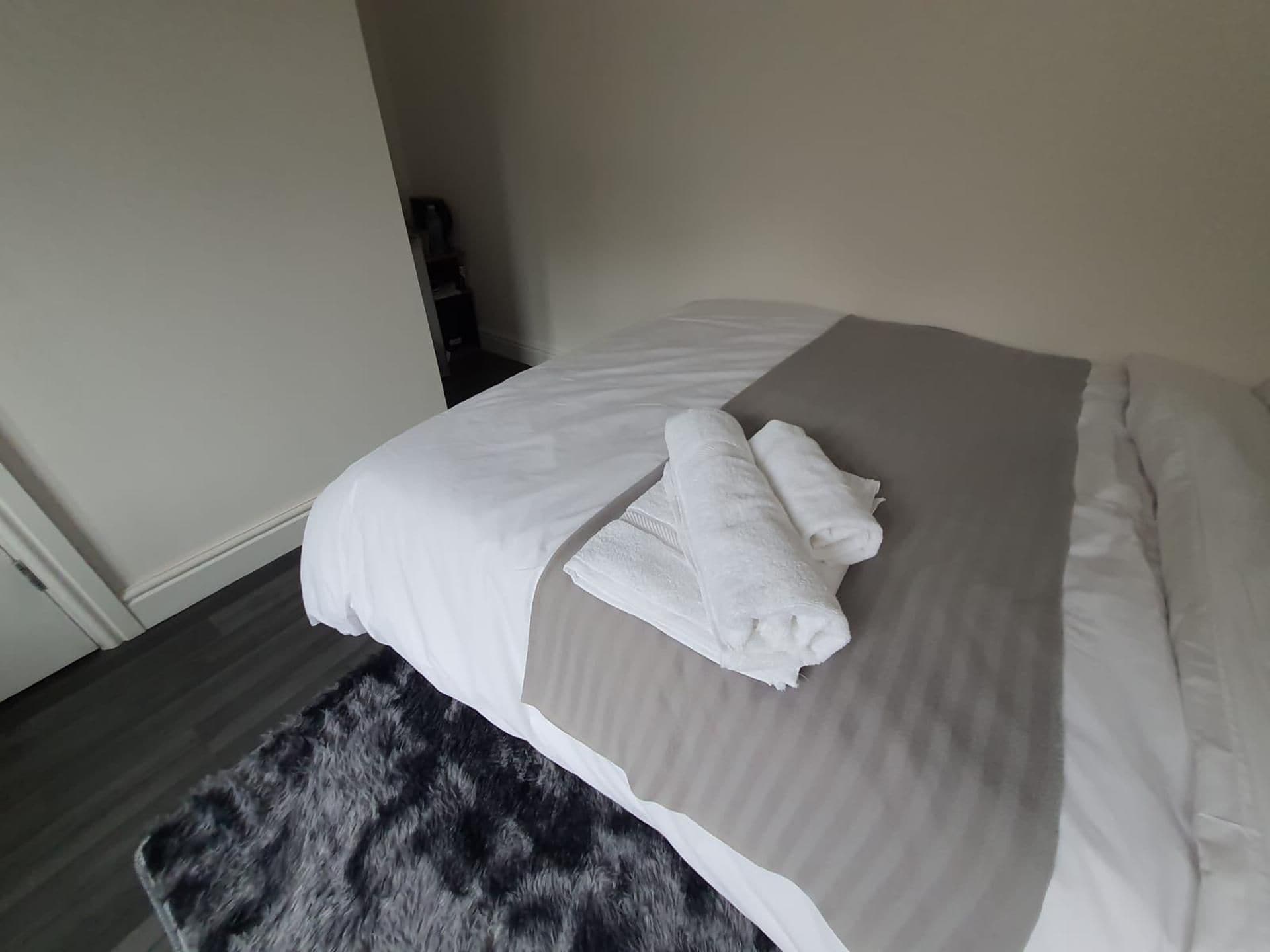Un lit bien fait, avec des draps blancs et deux serviettes pliées posées sur un couvre-lit gris.