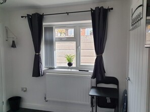 Una habitación con ventana, radiador, planta en maceta, una silla y un protector de radiador en el suelo.