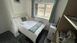 A bedroom with a bed, a desk, a chair, a window with curtains, a small plant, and a picture on the wall. - Private Room, Sleeps 2 With Ensuite & Parking (Birmingham)