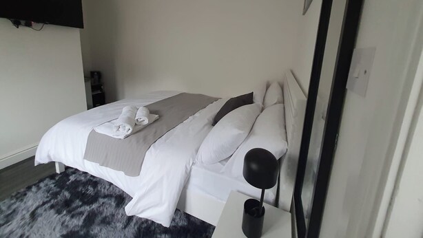 Ett modernt hotellrum med en snyggt bäddad säng, en svart golvlampa och en stor spegel.