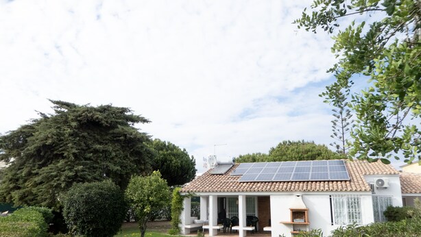 A house with a tiled roof, solar panels, a patio with outdoor furniture, and a garden.