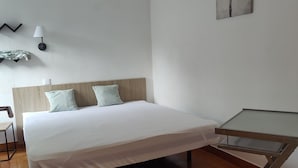 A bedroom with a bed, a desk, a chair, a lamp, and a painting on the wall.