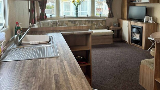 A compact RV kitchen with a sink, stove, and a small seating area. - 3 bed With Balcony on Lido Beach (Prestatyn)