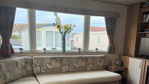 A cozy living room with a large sectional sofa, a small side table, a television, and a bookshelf. - 3 bed With Balcony on Lido Beach (Prestatyn)