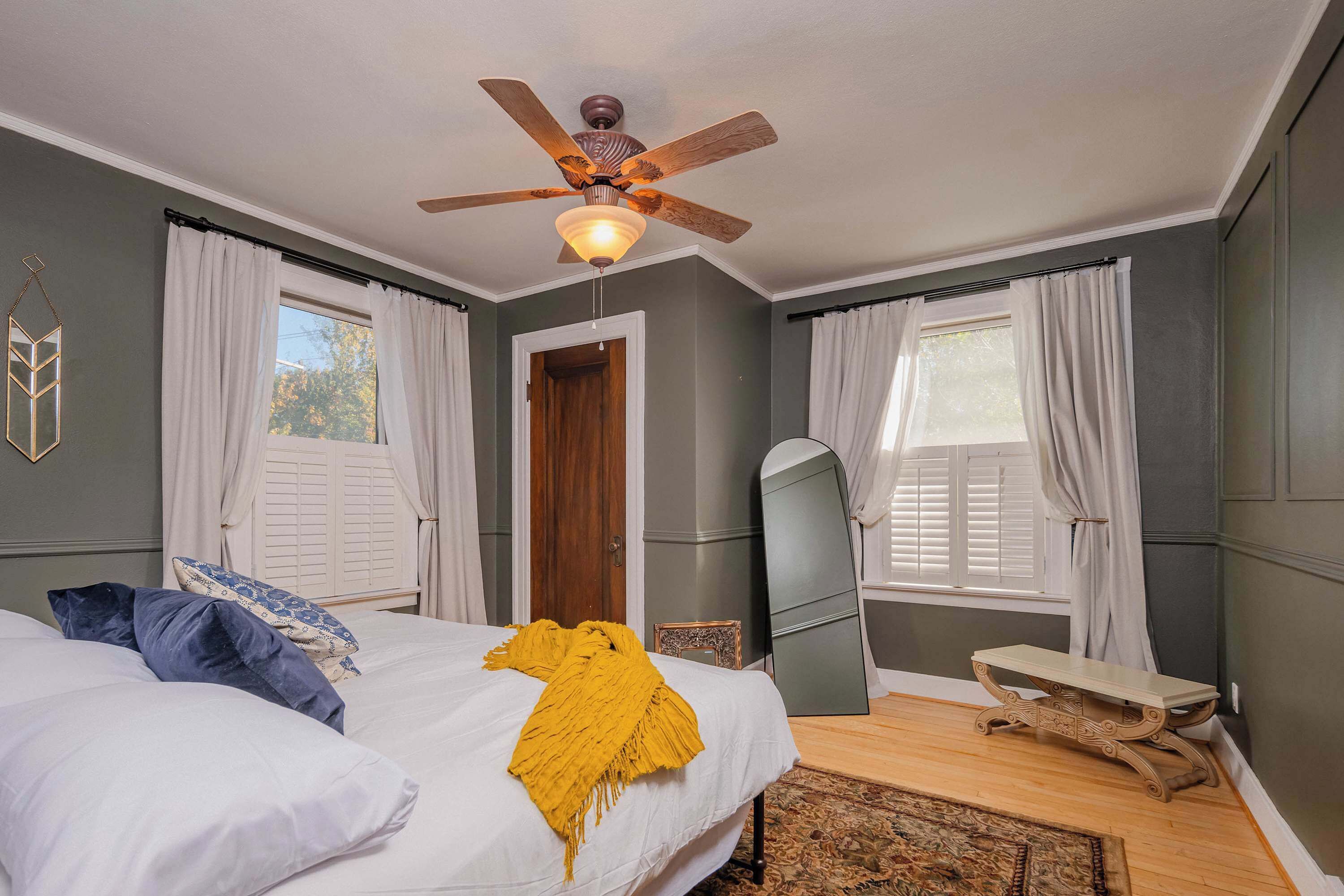 Quarto com uma cama, um ventilador de teto, um espelho e um banco.