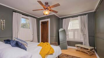 Quarto com uma cama, um ventilador de teto, um espelho e um banco.