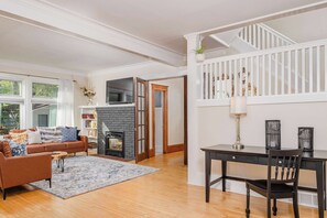 A living room with a fireplace, a sofa, a coffee table, and a dining table with chairs. - Third Ward Historic Mansion | Sleeps 13 (Appleton)