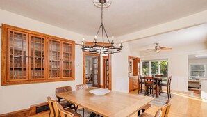 A spacious dining area with a large wooden table and chairs, a chandelier, and wooden cabinets with glass doors. - Historic Appleton Mansion-Sleeps 13 & Free Parking (Appleton)