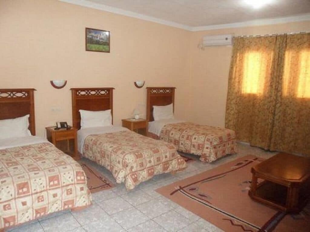 A hotel room with three beds, a small table, and a window with curtains.