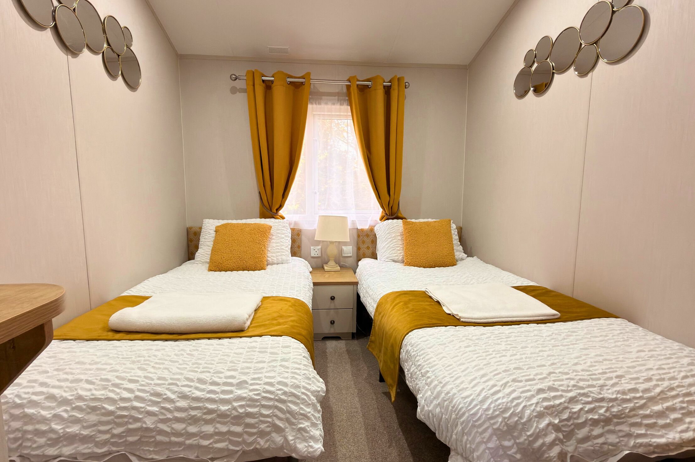 A room with two beds, a nightstand, a lamp, and a window with curtains.
