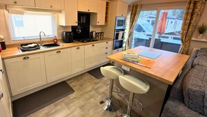 A modern kitchen with white cabinets, a wooden countertop, and two bar stools. - Meadows 33 Hot tub - Southview Holiday Park (Skegness)