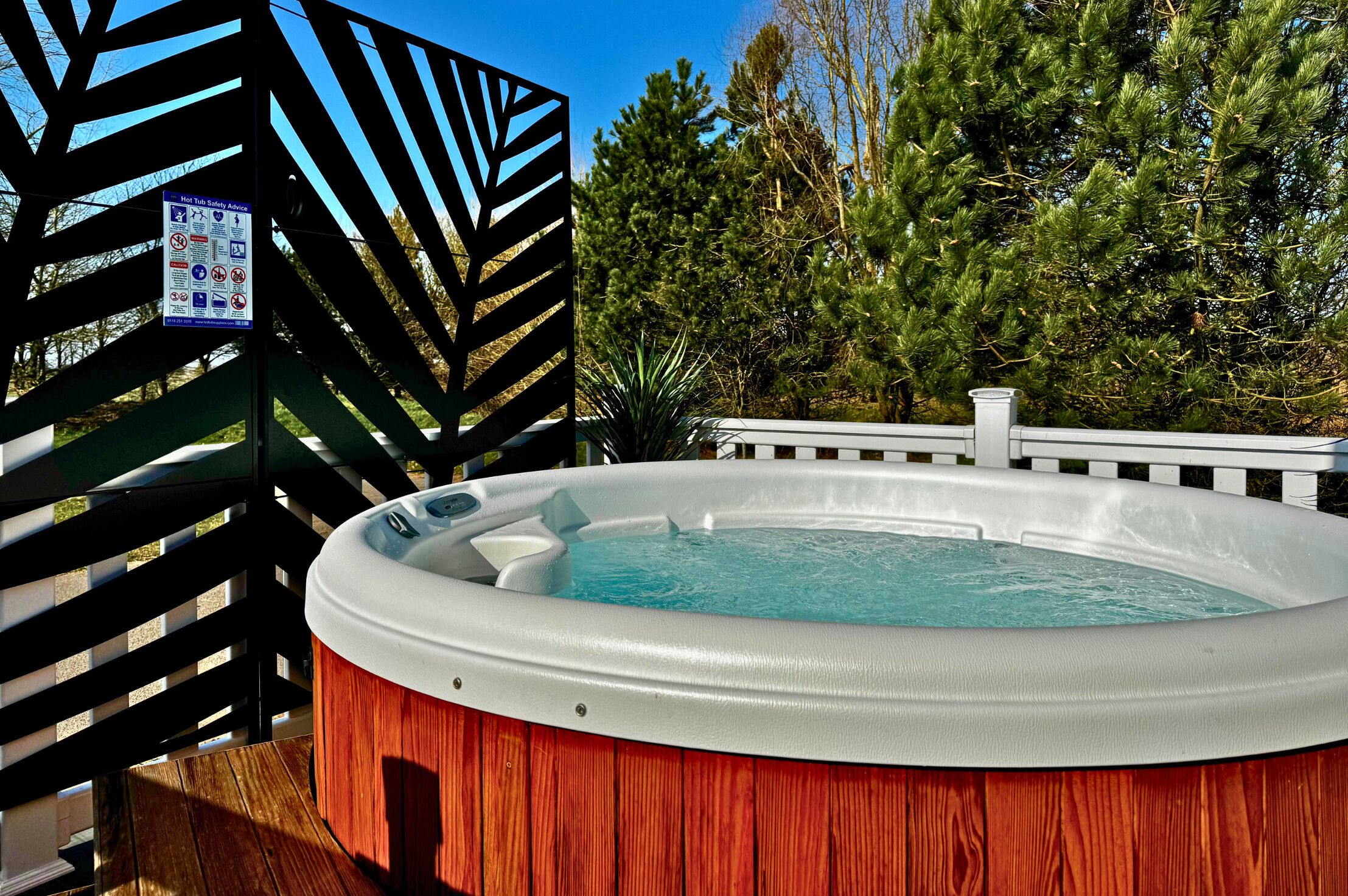 A hot tub surrounded by a wooden deck and a black metal fence.