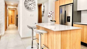Una cocina moderna con una isla central, armarios de madera, un refrigerador de acero inoxidable y un reloj de pared.