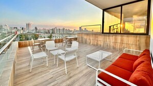 Un balcón moderno con vistas a la ciudad, que cuenta con piso de madera, sillas blancas, un sofá rojo y una mesa de vidrio.