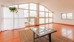 A spacious room with large windows, a hanging plant, and a glass-top table.