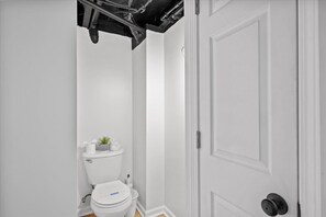 A small, white bathroom with a toilet, a small shelf with a plant, and a door with a round handle. - The Walnut Suites - The Incline Suite (Pittsburgh)