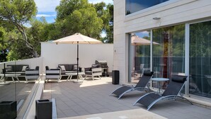 A modern outdoor patio with a glass balustrade, lounge chairs, a sofa, and a table. - Luxurious apartment in Postira (Postira)