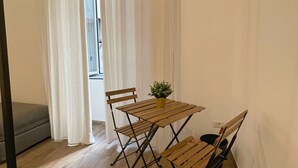 Un pequeño comedor con una mesa y sillas de madera, una planta en maceta y un sofá gris.