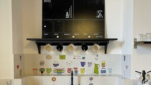 Cocina con un lavamanos blanco, armarios negros y una salpicadura trasera negra con baldosas que representan utensilios de cocina.