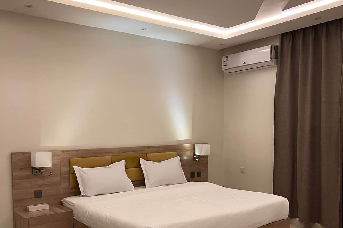 Een moderne hotelkamer met een groot bed, een houten hoofdeinde, nachtkastjes en een airconditioner.