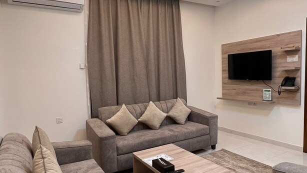 A modern living room with a grey sofa set, a coffee table, and a flat-screen TV mounted on the wall. - Sweet Star Serviced Apartments (Tabuk)
