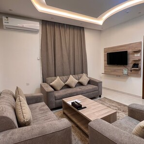 A modern living room with a grey sofa set, a coffee table, and a flat-screen TV mounted on the wall. - Sweet Star Serviced Apartments (Tabuk)