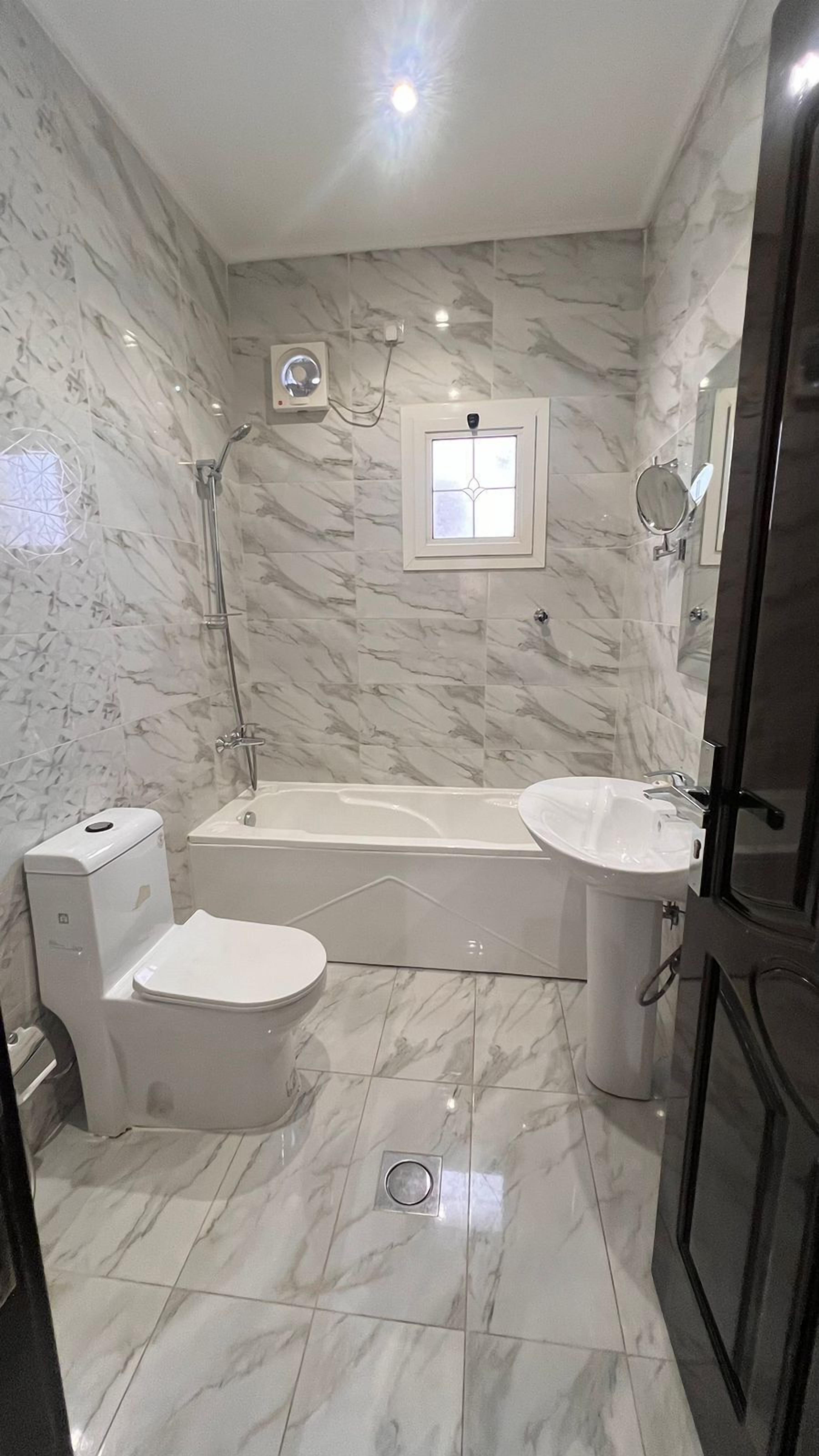 A bathroom with a bathtub, toilet, and sink, all with marble flooring and walls.