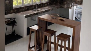 Una cucina con un piano di lavoro in marmo, una finestra con persiane e due sgabelli di legno.