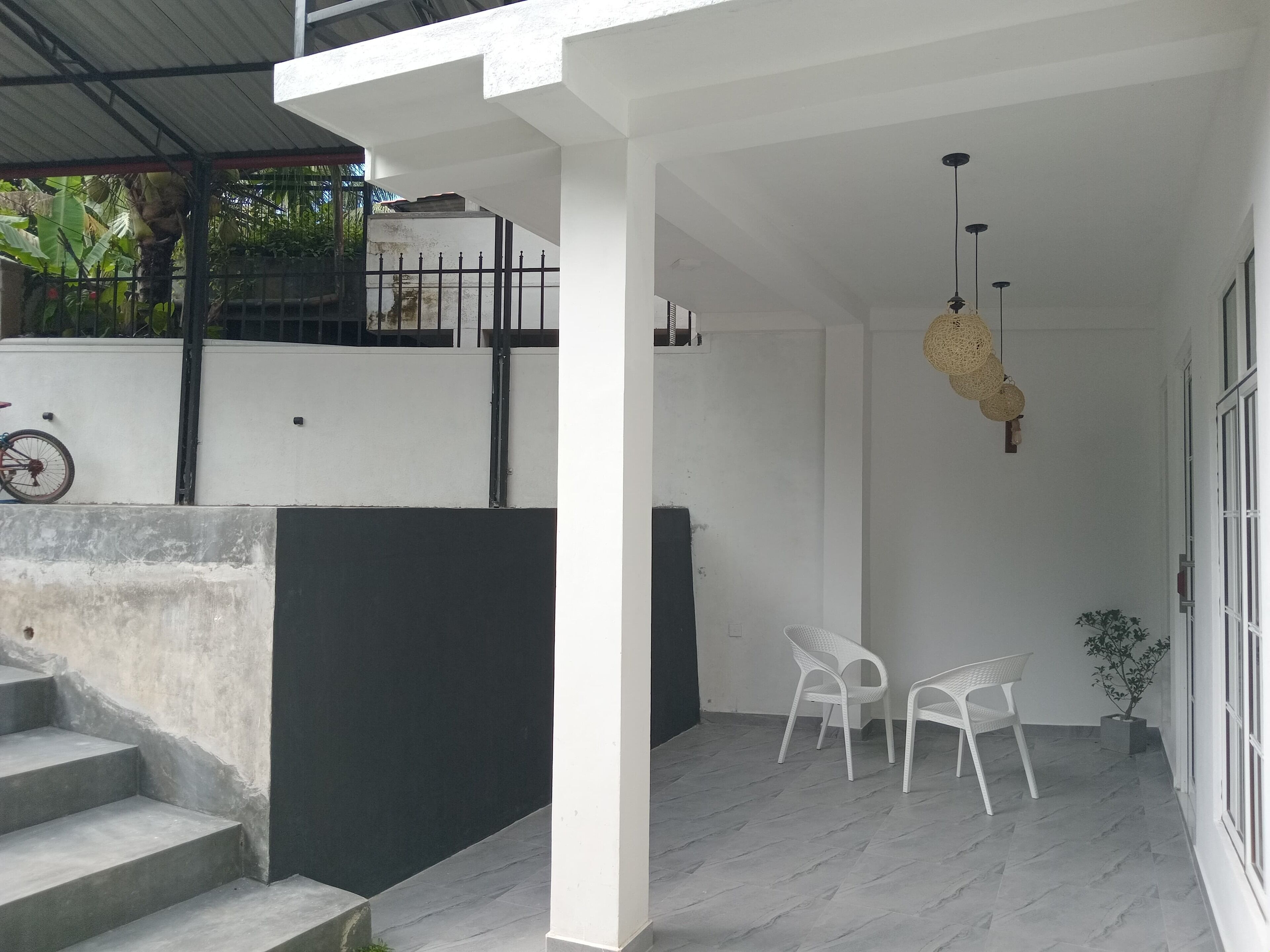 A covered outdoor area with a staircase leading to a higher level, white chairs, and a hanging light fixture.