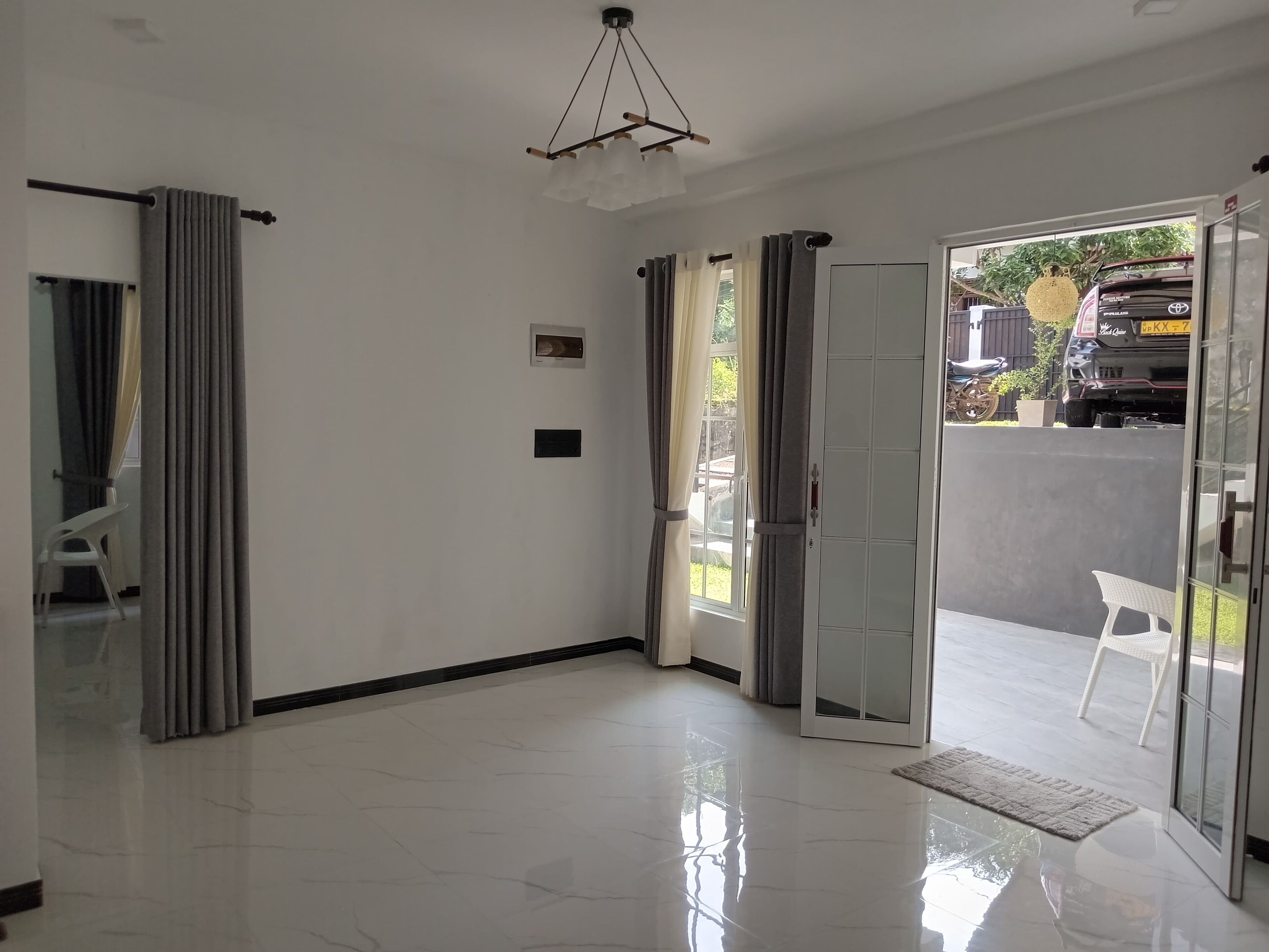 A spacious room with a large sliding glass door leading to a balcony, a ceiling light fixture, and a white tiled floor.