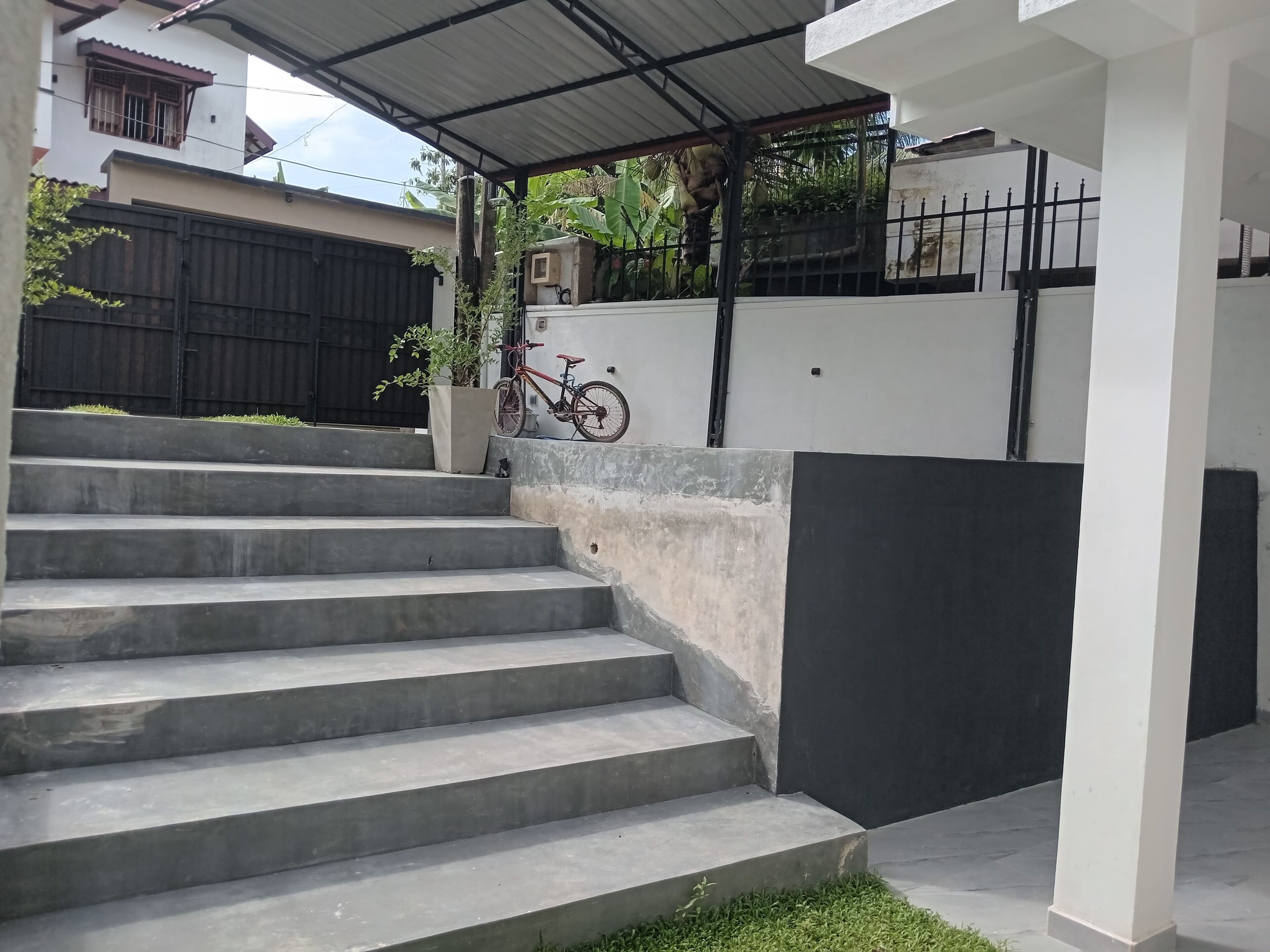 Unos escalones de hormigón llevan a un espacio exterior cubierto, con una bicicleta estacionada cerca.
