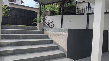 Unos escalones de hormigón llevan a un espacio exterior cubierto, con una bicicleta estacionada cerca.