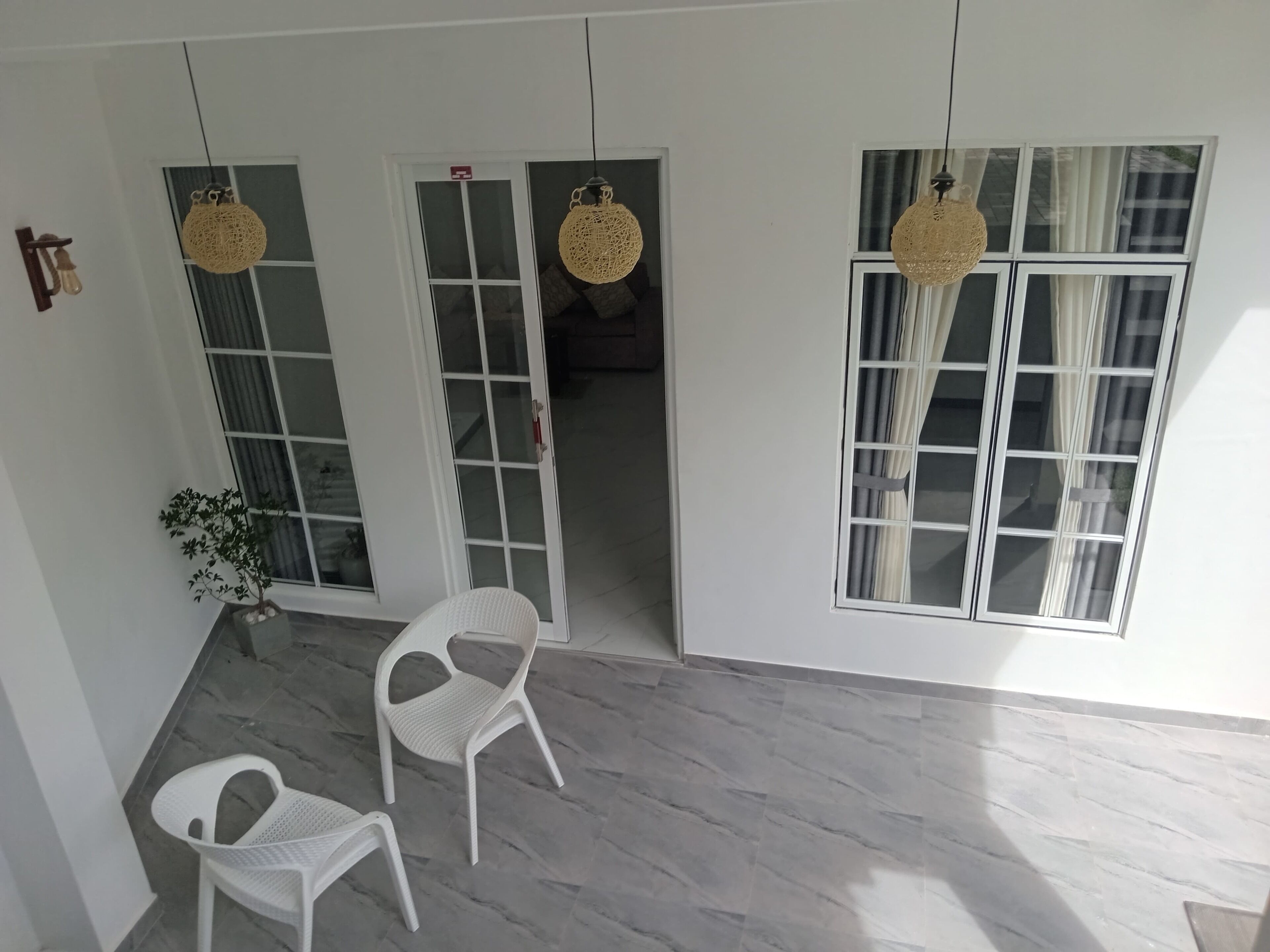 A room with white walls, two doors with glass panels, a potted plant, two white plastic chairs, and hanging woven light fixtures.