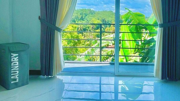 Una stanza con un'ampia porta-finestra scorrevole che si apre su un balcone con vista su una vegetazione rigogliosa e un cielo sereno.