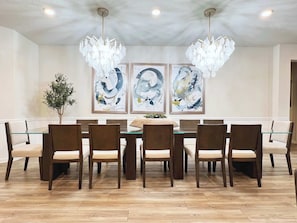 Un'area pranzo con un tavolo in vetro circondato da sei sedie, un lampadario e arte astratta appesa al muro.