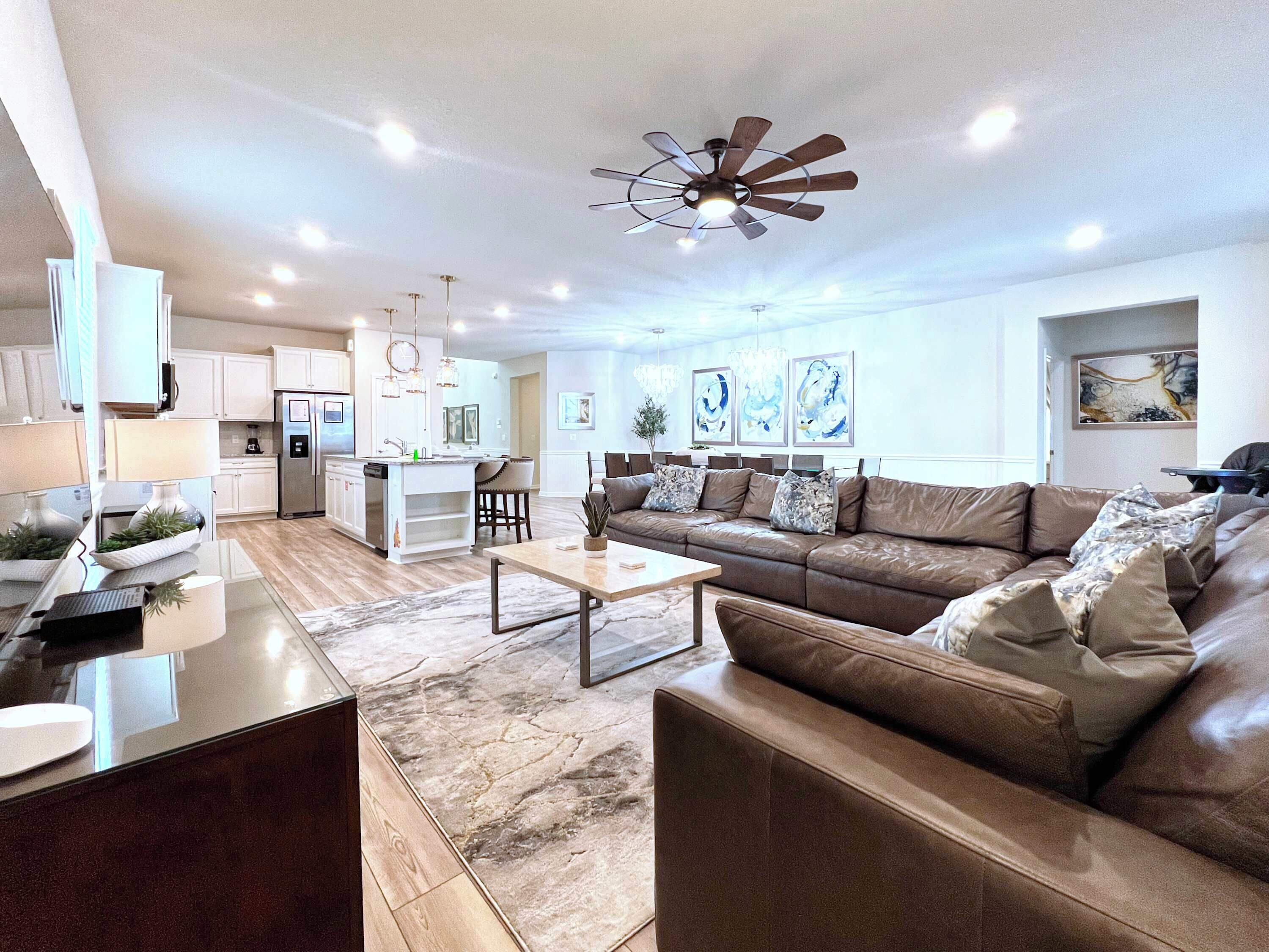 A modern living room with a brown leather sofa, a coffee table, and a kitchen area in the background.