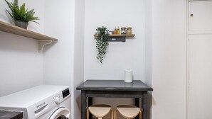 A compact laundry room with a washing machine, a small table with two chairs, a shelf with plants and jars, and a door. - Starry Nights - Elegent Studio in Athens (Greece - Athens)