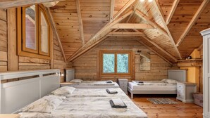 Uma cabana com quarto no mezanino, vigas de madeira, uma janela grande e uma cama de casal com duas mesas de cabeceira.