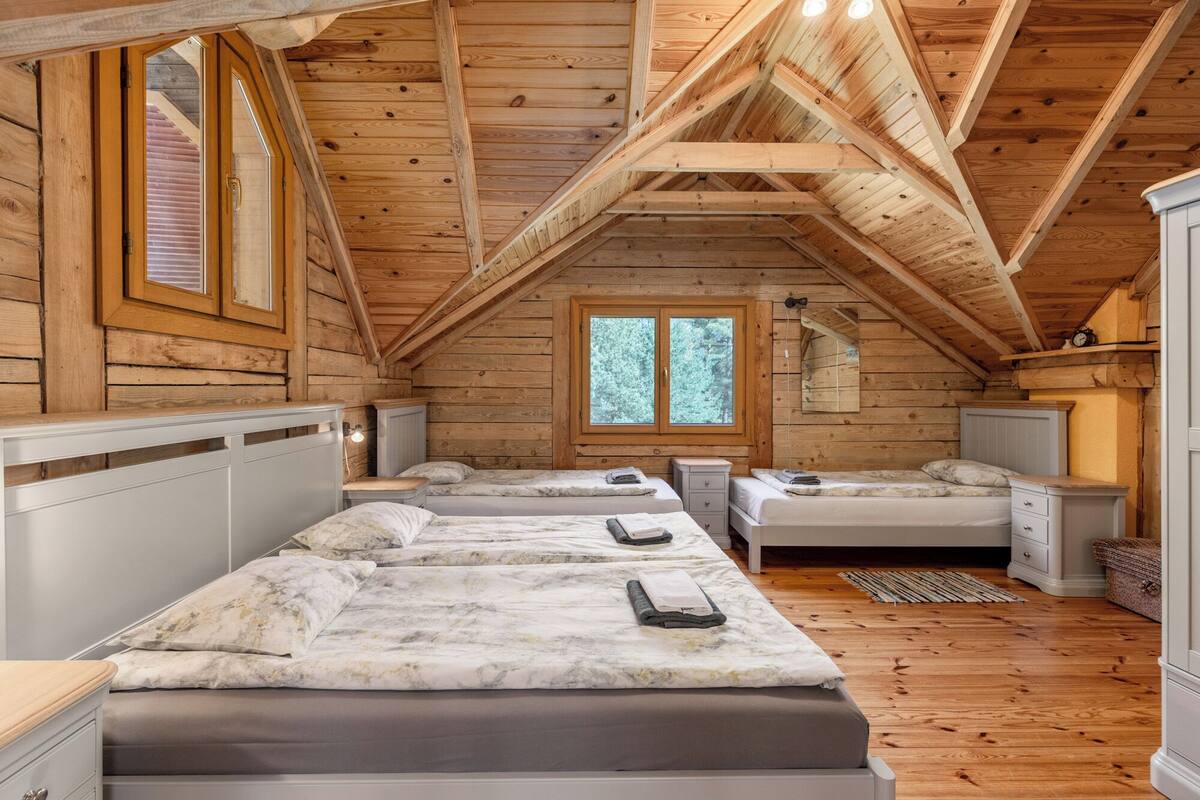 Een chalet met slaapkamer op entresol, zichtbaar met houten balken, een groot raam en een lang bed met twee nachtkastjes.
