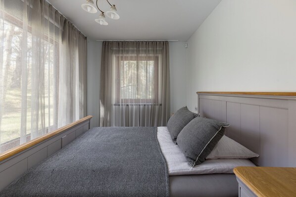 A bedroom with a bed, a wooden headboard, a window with sheer curtains, and a ceiling light fixture.