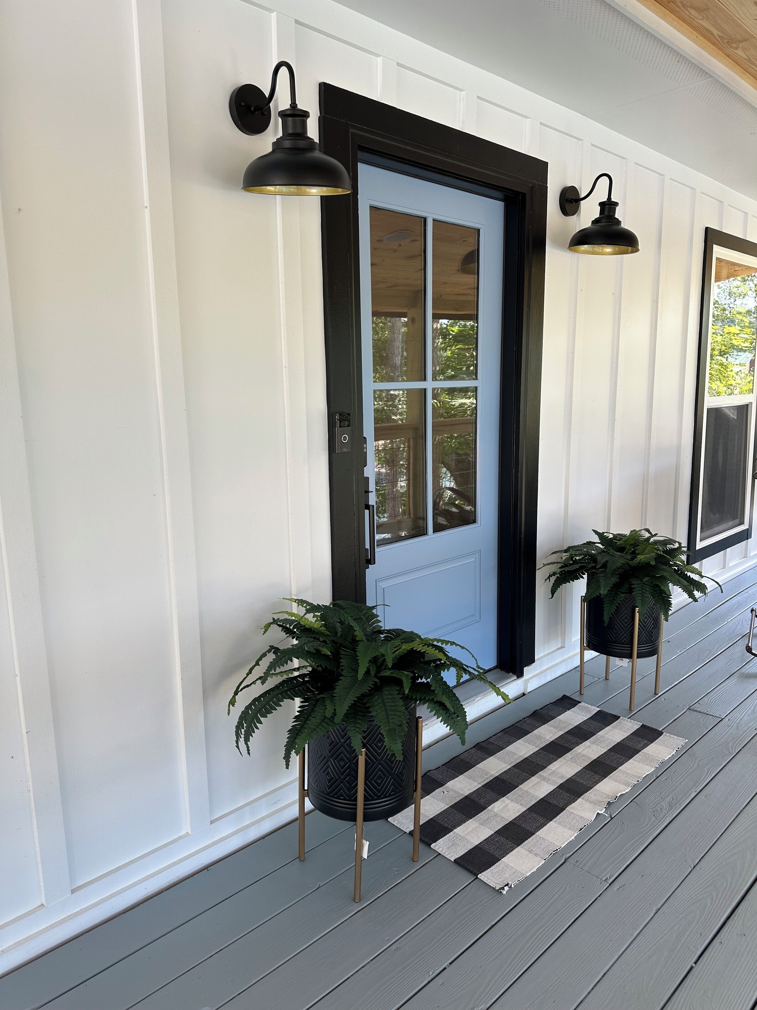 A front porch with a blue door, two wall-mounted lights, and two potted plants.