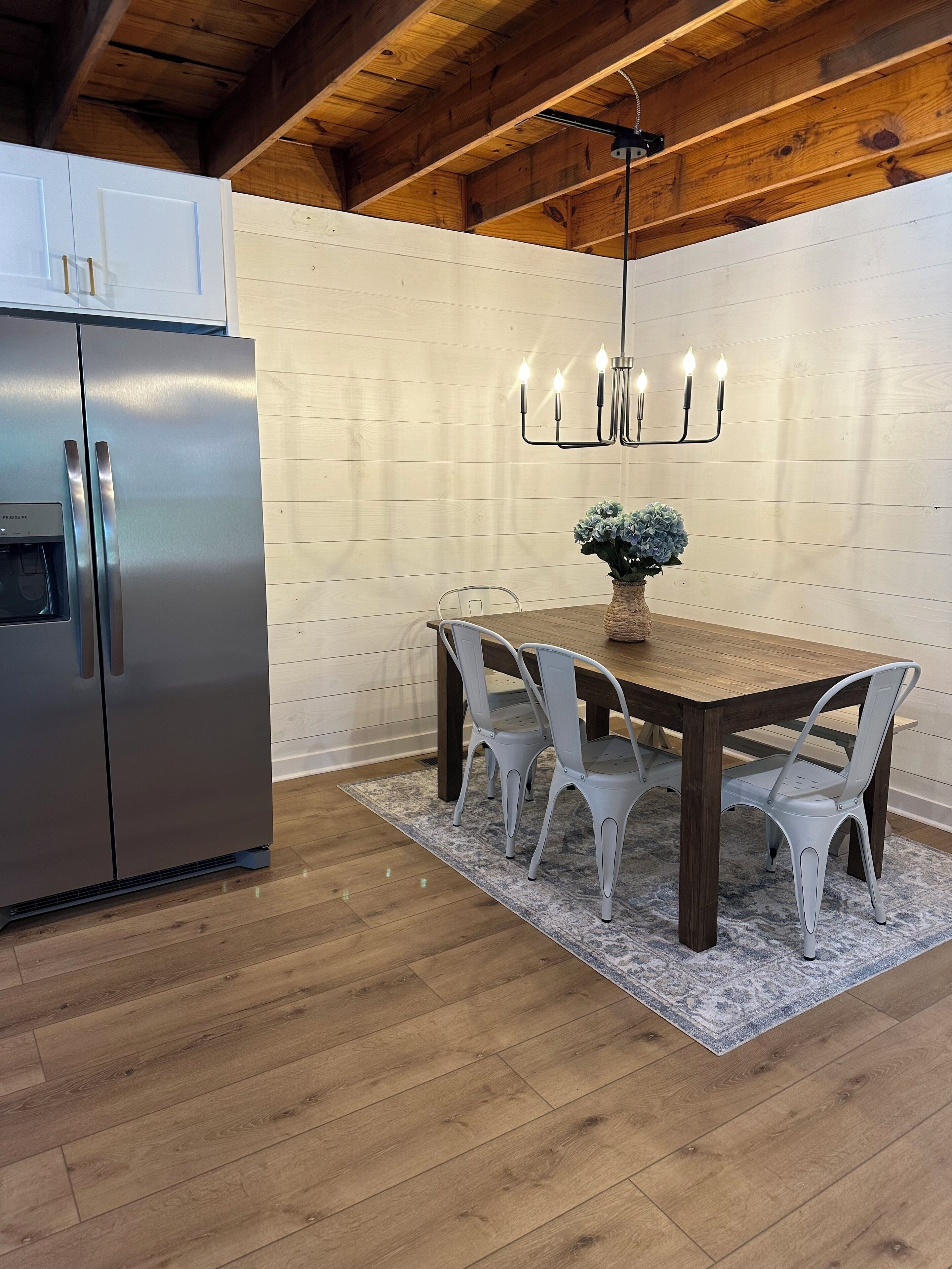 Une cuisine moderne avec un réfrigérateur en acier inoxydable, une table à manger en bois avec quatre chaises et un chandelier avec des bougies.