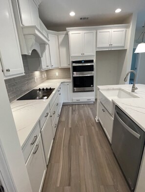 A modern kitchen with white cabinetry, a built-in oven, a stovetop, and a dishwasher.